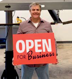 Helical Solar team member holding an Open for Business sign in a workshop
